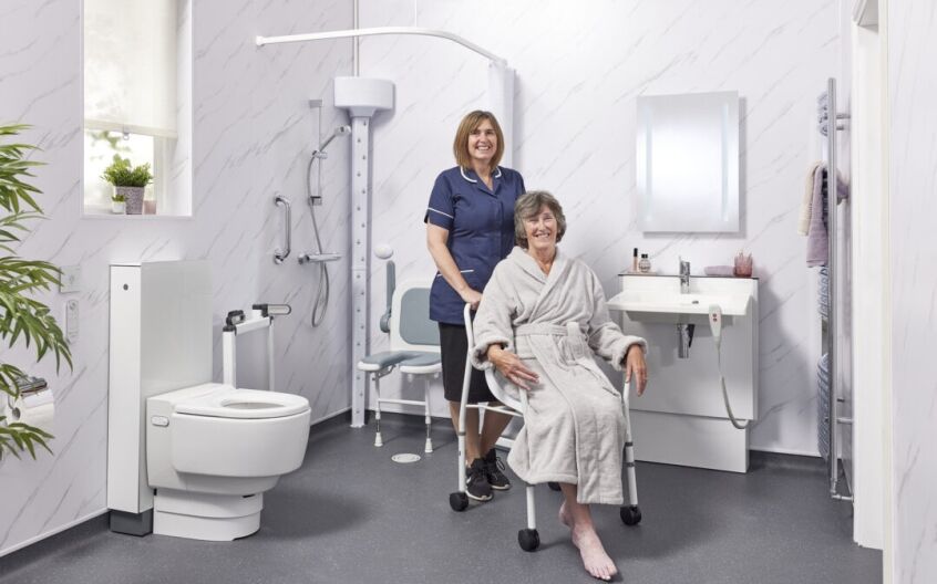 Carer assisting elderly lady in luxury accessible wet room with smart toilet and body dryer