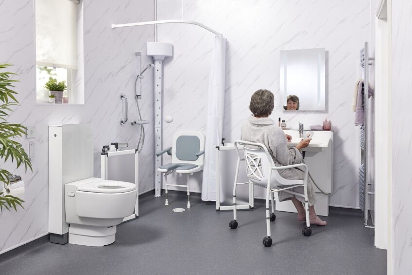 Elderly woman using a mobile shower chair in a small accessible wet room with grab rails