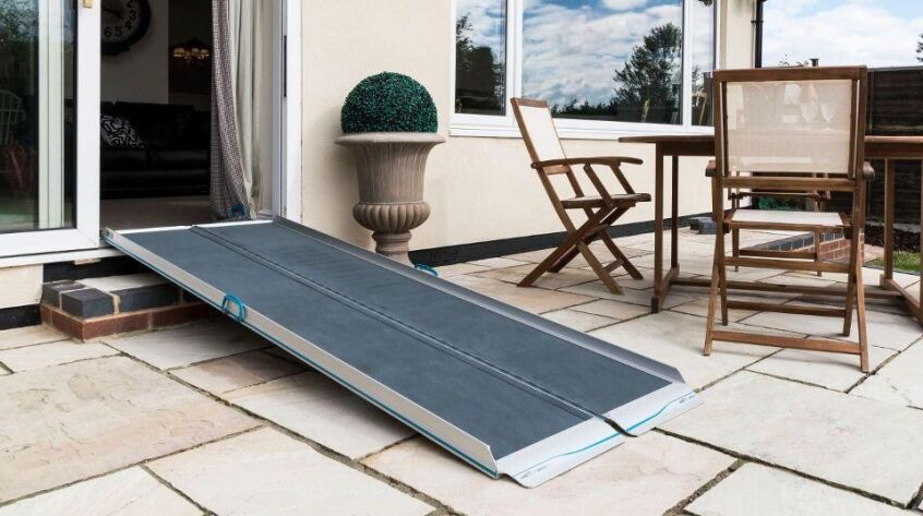 Portable aluminium wheelchair ramp bridging the step from patio doors to a garden patio