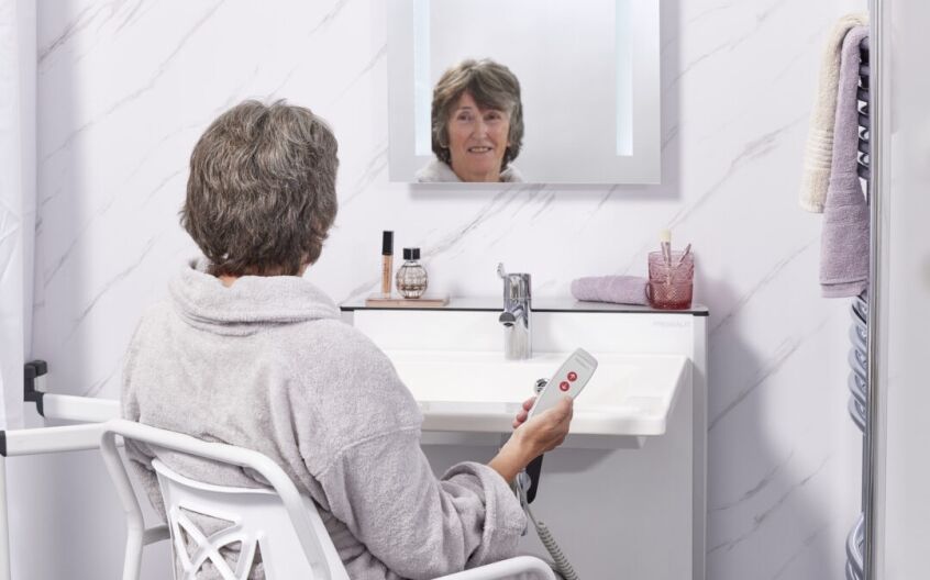 Older woman seated in a wheelchair at a wall-hung accessible basin with knee space
