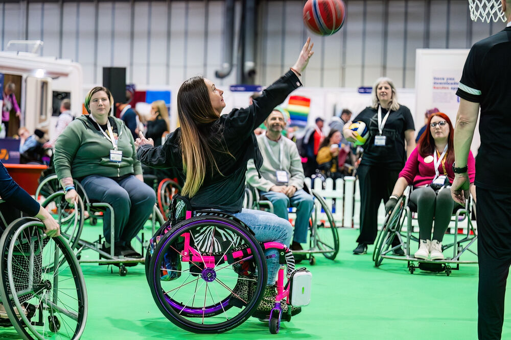 Older woman in bathrobe standing beside level-access shower with fold-down seat, grab rails, and anti-slip blue flooring in accessible bathroom